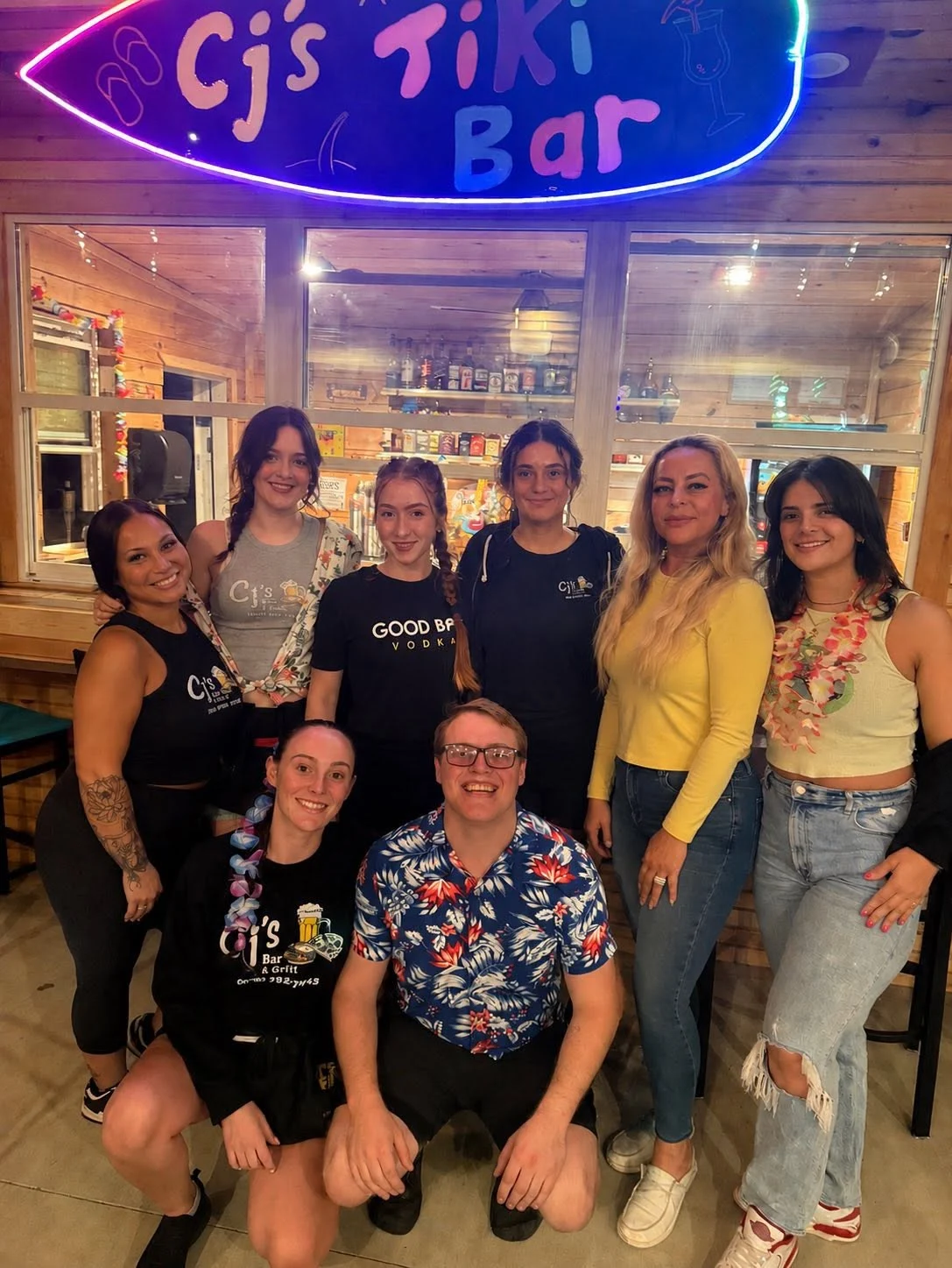 The CJ’s team together in front of the tiki bar sign